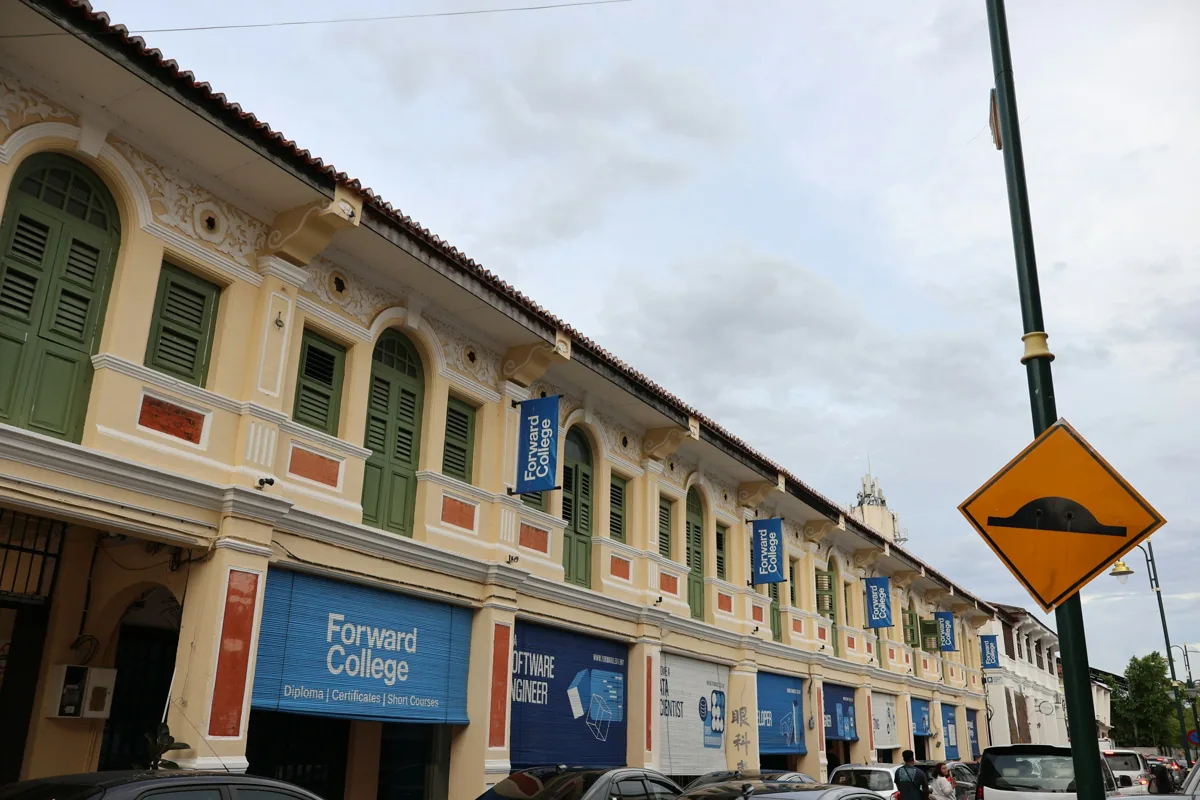 A row of George Town shophouses with green shutters and sheltered walkways