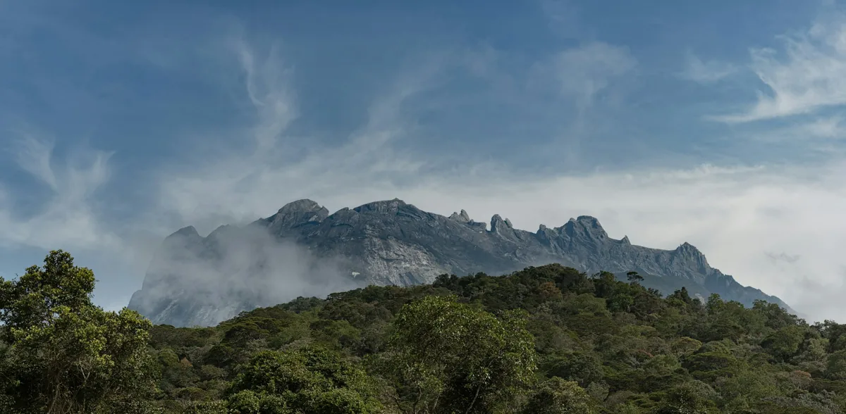 The granite ridgeline of Mount Kinabalu behind forested hills in Sabah